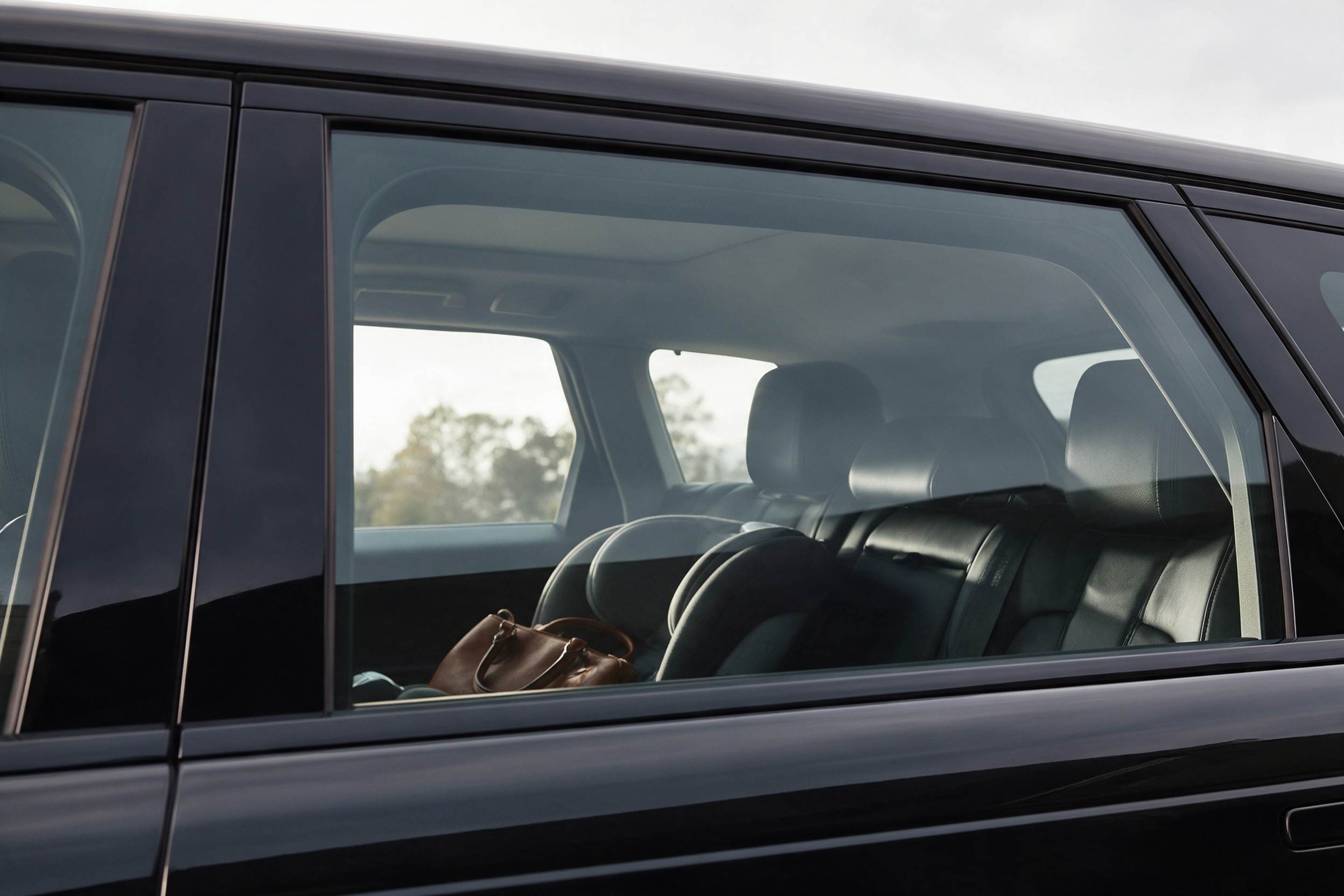 Hintere Seitenscheibe eines schwarzen SUV bei Tag, durch das klare Glas sind Kindersitz, Handtasche und Rücksitzbank zu sehen
